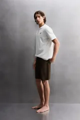 Camiseta blanca de corte holgado confeccionada en tejido de algodón con elasticidad. Tiene cuello redondo, manga corta y estampado en el frente con el logo de la marca y un diseño de tablas de surf.