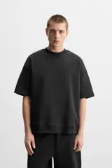 Sudadera negra de corte relaxed fit, confeccionada en tejido interlock de algodón con elasticidad. Tiene cuello redondo, manga corta y bajo acabado en rib.