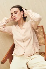 Camisa marrón de manga larga con escote en V y botones forrados al tono en el frente. Destaca por su textura sutil y por el detalle de frunces con volados en la parte inferior.