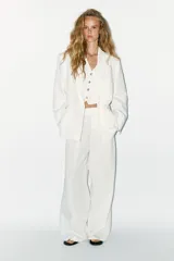 Blazer oversize color blanco confeccionado con 22% de lino. Tiene cuello solapa, manga larga con hombreras y abertura en la espalda. Incluye cinturón lazada en el mismo tejido.