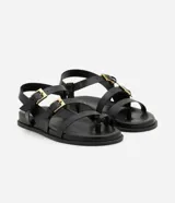 Sandalias negras con tiras de cuero sintético, suela plana y hebillas doradas.