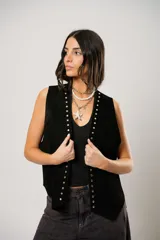 Chaleco negro de cuero descarne con terminación en picos, tachas metálicas y flecos en la espalda.