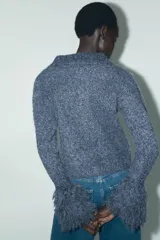 Chaqueta de punto azul con cuello solapa, manga larga y flecos en las mangas. Cierre frontal con botones.