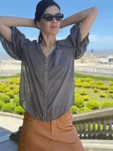 Camisa de gasa color gris oscuro, con mangas globo y una tira central vertical decorada con piedras azules.