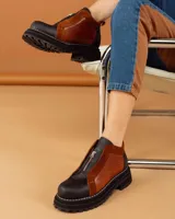 Botines de cuero negro con paneles laterales de charol, cierre frontal con cremallera y suela track.