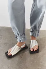 Sandalias plateadas de cuero con tira ancha sobre el empeine y tira que separa el dedo gordo. Suela plana cuadrada color negro y tira trasera elástica.