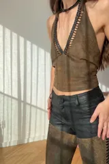 Top marrón de cuero ovino vintage con cuello halter, espalda descubierta y cierre con lazos. Presenta detalle artesanal de cutouts y pasamanería en negro alrededor del cuello.