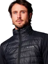 Chaqueta híbrida Columbia para hombre, color negro. Presenta un cuerpo acolchado con aislamiento Thermator reciclado y mangas de tejido softshell elástico y transpirable. Tiene cuello alto, cierre frontal completo y bolsillos laterales con cremallera.