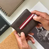 Billetera marrón de símil cuero con galón elastizado a rayas rojas y blancas. Interior con doble repartición para billetes, visor y tarjeteros.