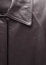Abrigo largo oversize de cuero ovino color marrón oscuro, con cuello camisero, cierre frontal oculto con cremallera, mangas largas con puños abotonados, forro interior y dos bolsillos laterales.