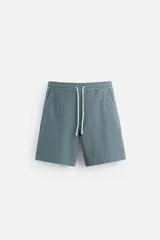 Bermuda azul de tejido con mezcla de algodón, corte relaxed fit, cintura elástica ajustable con cordón, bolsillos delanteros y detalle de bolsillo trasero de vivo.