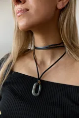 Collar con doble tira de tiento negro, una ajustada al cuello como choker y otra más larga con un dije ovalado de piedra natural blanca y un pequeño detalle dorado.