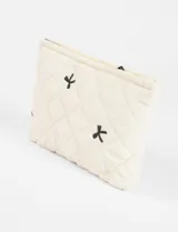 Estuche acolchado color crema con diseño de moñas bordadas en negro y cierre superior.