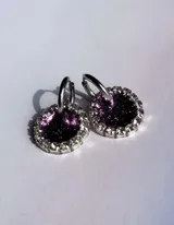 Aros colgantes con forma circular, hechos de resina color lila y borde de strass plateado. El aro es de acero quirúrgico plateado.