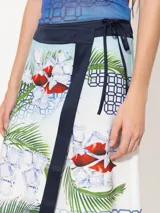 Pollera tipo portafolio de satén con estampado de palmeras, cubos de hielo y labios rojos. Tiene cinta para anudar en la cintura, botón interno y zócalo de tela complemento en cintura y ruedo.