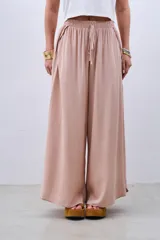 Pantalón palazzo color beige de fibrana con cintura elastizada y cordón ajustable. Presenta aberturas laterales desde la cadera.