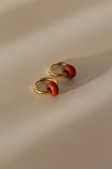 Par de aros tipo argolla dorados con dije de piedra natural con patrón de manchas negras sobre fondo blanco.