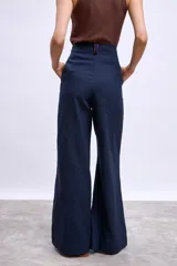 Pantalón ancho de tiro alto color azul marino, con pliegues frontales y ribetes en color naranja quemado en los bordes del bolsillo y la cintura.