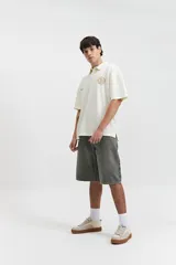 Remera polo color beige con textura acanalada, corte oversize, cuello clásico con botones y logo estampado en el pecho.