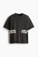 Remera negra de corte holgado con cuello redondo y mangas cortas. Estampado frontal con la inscripción "ORK XON NEW THE".