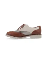 Zapato Oxford de cuero color cognac, blanco y plateado, con cordones marrones, detalles de perforaciones y suela de goma blanca.