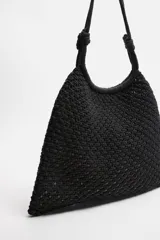 Bolso tipo shopper negro, confeccionado en tejido trenzado de algodón con diseño de red. Cuenta con dos asas de hombro ajustables que funcionan como cierre del compartimento principal.