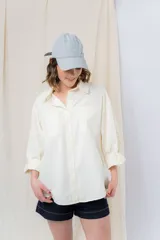 Camisa color crema de algodón liviano, calce oversize, con bolsillos frontales con solapa, cierre con botones y mangas largas que se pueden arremangar.