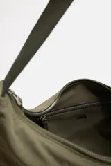 Bolso de hombro color verde oliva, fabricado en tejido técnico acolchado. Tiene un compartimento principal con cierre de cremallera, un bolsillo interior con cremallera y un bolsillo frontal con cremallera. El asa de hombro es ajustable.