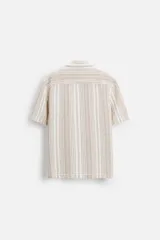 Camisa de manga corta con cuello bowling y corte relaxed fit. Diseño a rayas verticales en tonos beige y blanco. Cierre frontal con botones y bajo con aberturas laterales.