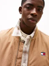 Chaleco de lona color marrón claro con capucha, cierre frontal con cremallera, dos bolsillos delanteros ribeteados, un bolsillo interior y parche con logo de Tommy Jeans en el pecho.