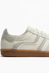 Championes deportivos color crema con detalles en gris y suela marrón. Presentan collarín acolchado, cordones y logo bordado en el lateral. Grosor de la suela 2,5 cm.