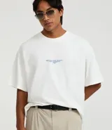 Remera de algodón blanca, corte oversized, con cuello redondo y manga corta. Presenta un pequeño estampado de texto en color azul claro en el pecho.