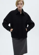 Chaqueta corta negra de mezcla de lana con cuello camisero, cierre frontal con cremallera, bolsillos laterales y mangas largas con puños abotonados.