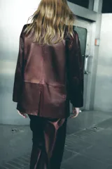 Blazer de cuero color marrón chocolate con cuello solapa, cierre frontal con dos botones, bolsillos de vivo y abertura en la espalda.