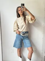 Bermuda de jean celeste de corte ancho, con cintura alta y largo a la rodilla. Presenta ruedo desflecado y se complementa con un cinturón ancho de cuero negro con tachas plateadas.