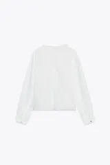 Camisa blanca de cuello subido y manga larga, con detalle de entredós combinados a tono y cierre frontal con botones.