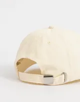 Gorra de béisbol color crema, de tela canvas, con visera curva y bordado frontal con la frase "Wanted Something More" en letras color lila y amarillo.