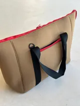 Bolso tote de neopreno negro con cierre superior y bolsillo externo con cierre verde. Tiene asas de mano marrones con bordes naranja, bolsillo interno y monedero haciendo juego.