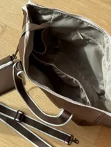 Bolso tipo tote de neopreno color negro y marrón, con cierre superior, bolsillo frontal marrón con logo rojo, bolsillo interno y externo con cierre, doble asa de mano marrón con detalles blancos y opción de correa larga.