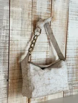 Bolso de hombro color blanco con textura craquelada, asa corta con eslabones dorados y asa larga con nudo decorativo.