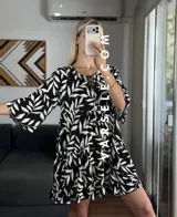 Vestido corto color verde oliva con estampado de hojas en blanco y negro, escote con lazo ajustable y mangas 3/4 acampanadas.