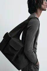 Bolso shopper negro de hombro fabricado en tejido técnico. Tiene un compartimento principal sin cierre, un bolsillo plano y otro con cierre mediante cremallera en el interior. En la parte frontal tiene dos bolsillos con cierre mediante imán y asa de mano.