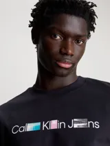 Remera negra de algodón con cuello redondo y mangas cortas. Estampado frontal con el logo de Calvin Klein Jeans en letras blancas con detalles fotográficos en colores celeste, rosa y gris.