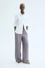 Pantalón recto de tela vaporosa a rayas verticales blancas sobre fondo gris. Tiene corte holgado, cintura elástica con cordón de ajuste, bolsillos laterales y traseros insertados.