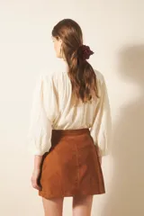 Minifalda de cuero gamuzado color marrón, con flecos y broches tipo snap en el centro delantero. Presenta tachas metálicas y remaches símil piedra a lo largo de la línea de los flecos.