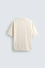 Camiseta color crema de corte holgado, confeccionada en tejido con textura arrugada y cuello redondo.