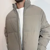 Campera puffer color beige con cierre frontal y cuello alto. Diseño acolchado con bolsillos laterales.