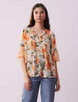 Blusa de gasa estampada con flores color naranja, marca Figueroa & Flower. Tiene cuello a la base, escote en V con lazo, abertura central con botones, delantera plisada y mangas 3/4 amplias.