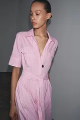 Vestido camisero midi de popelina a rayas verticales rosas y blancas, con cuello solapa, manga corta, bolsillos de parche en el pecho, cinturón de lazo ajustable y cierre frontal con botones.