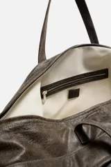Bolso de viaje marrón oscuro fabricado en piel con acabado craquelado. Tiene un compartimento principal con cierre de cremallera, un bolsillo plano interior con cremallera y dos bolsillos frontales con botón a presión. Cuenta con asas de mano de piel y asa de hombro removible y ajustable.